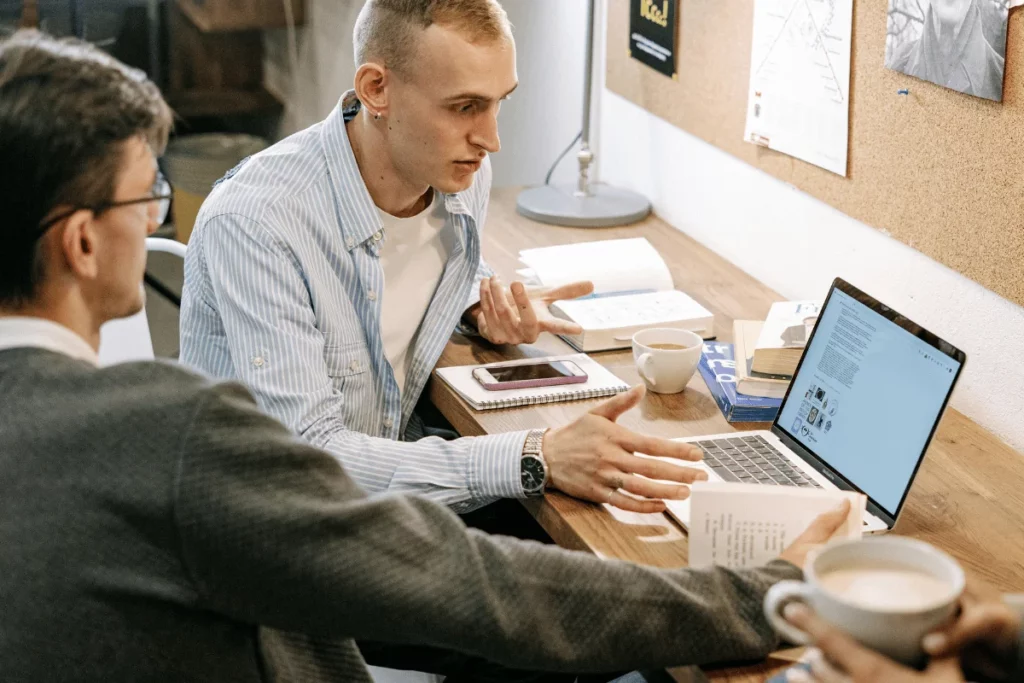 Two men discussing something while reviewing a laptop screen.