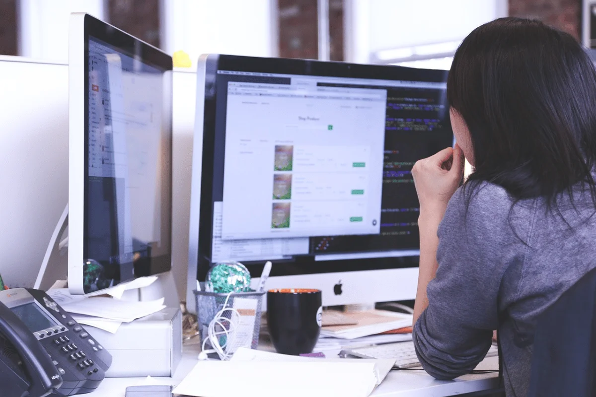 Person at a desk with two monitors displaying a code editor and a web interface.