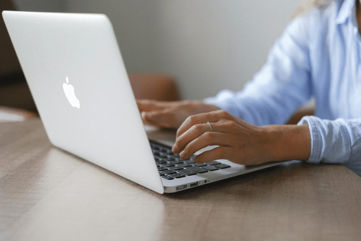 Hands on MacBook keyboard, working on business tasks.