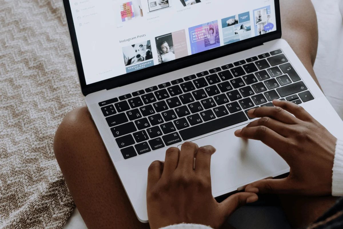 Person designing social media content on a laptop while sitting on a bed, with hands on the keyboard and templates visible on the screen.