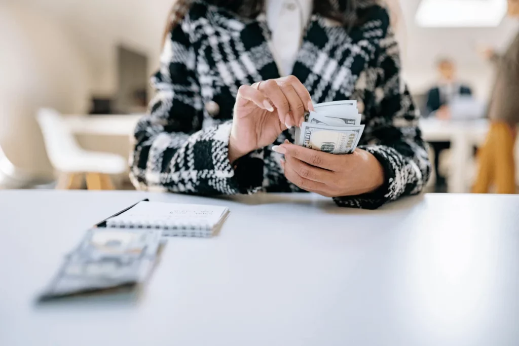 Individual in a checkered coat counting money at a table.