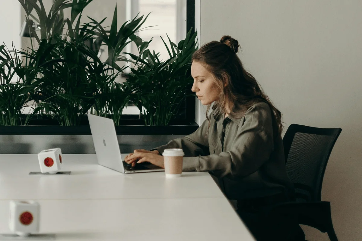 A woman typing on a laptop in a modern office space with green plants.