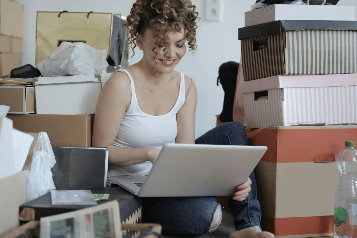 Person sitting on the floor among boxes, using a laptop.