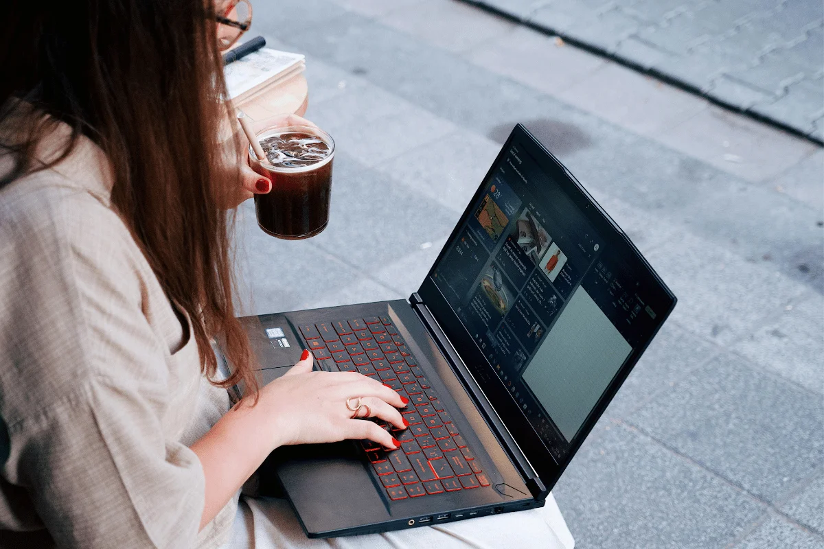 Side view of a woman working on a laptop with an iced coffee in hand.