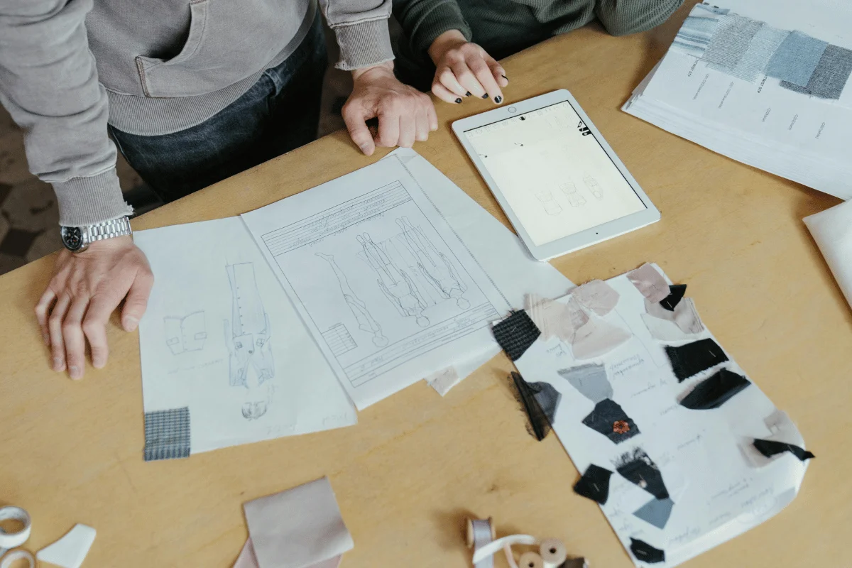 Fashion designers reviewing garment sketches and fabric swatches on a table.