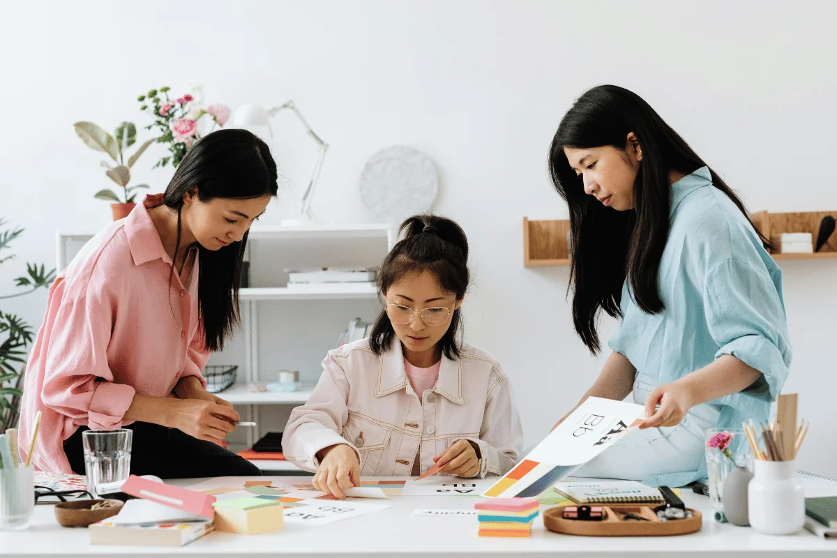 Three women collaborating on a creative project, working together on design ideas at a desk.