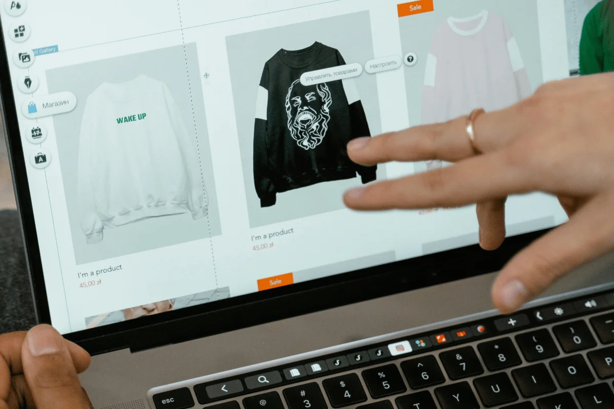 Hands pointing at laptop screen displaying sweatshirts in online store.