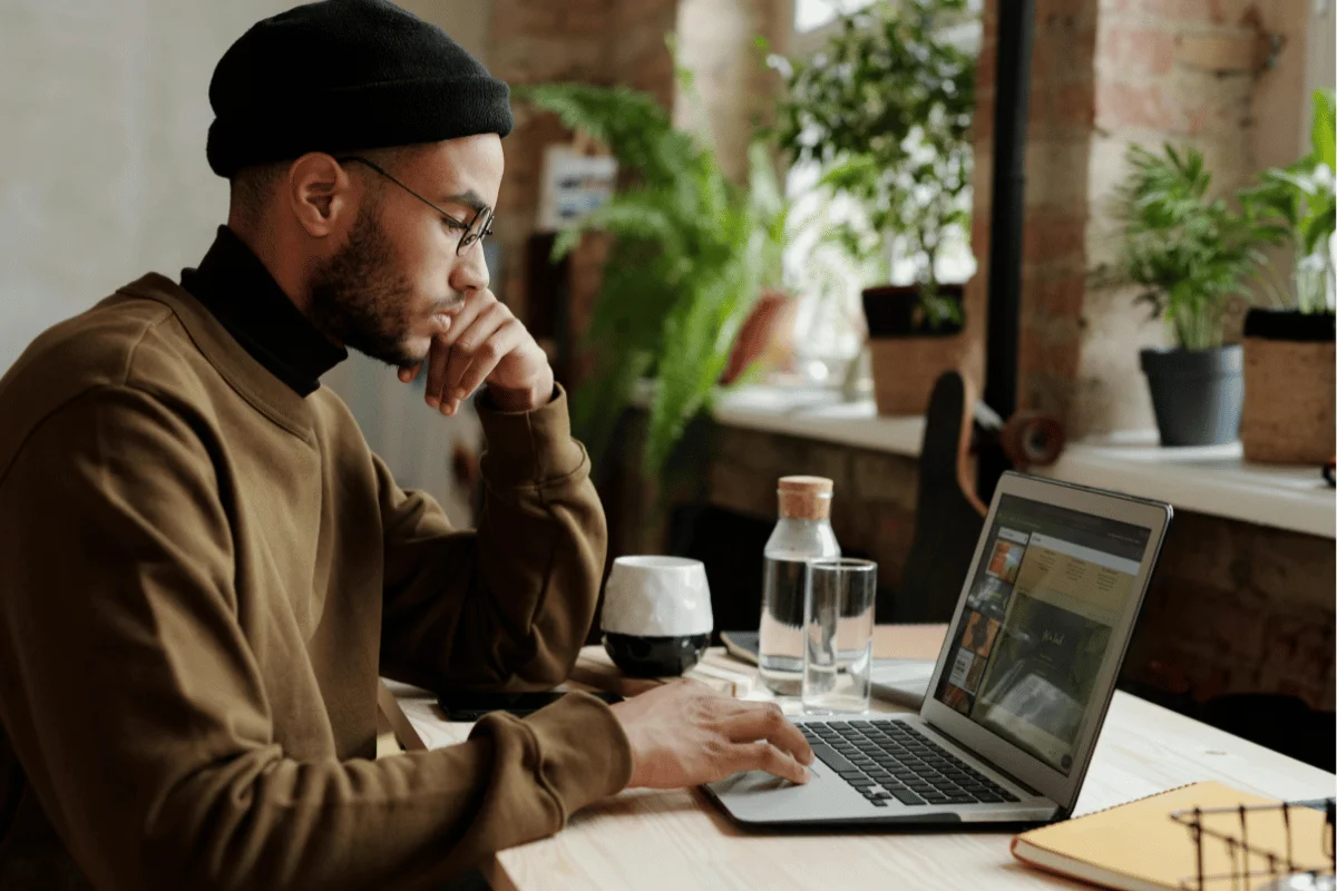 Man concentrating on his laptop in a well-lit, plant-filled home office.
