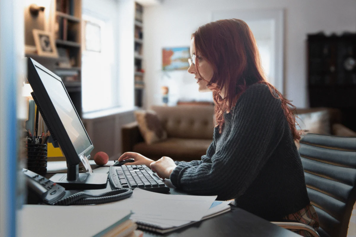 Woman working remotely from home office on desktop computer.
