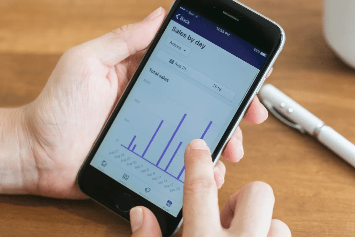 A person analyzes sales data on a smartphone, displaying a graph with daily sales statistics in a clean, user-friendly interface.