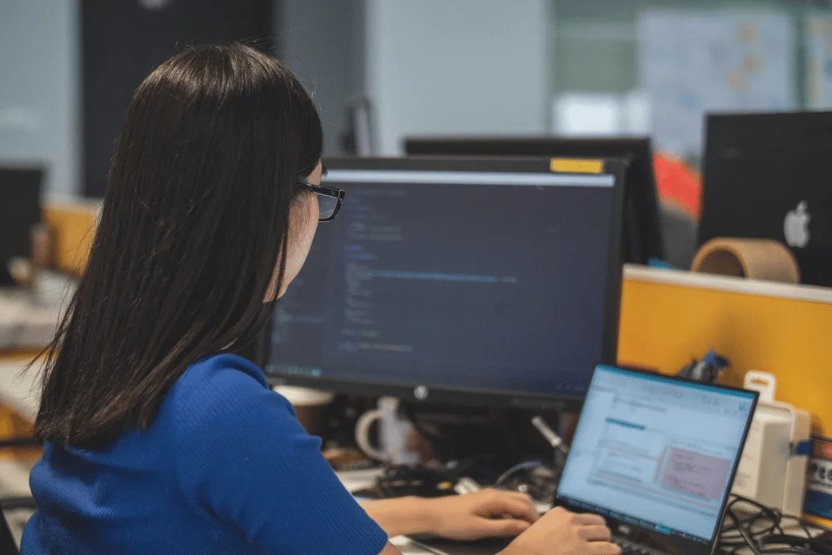 A person working at a desk with two monitors, displaying lines of code.