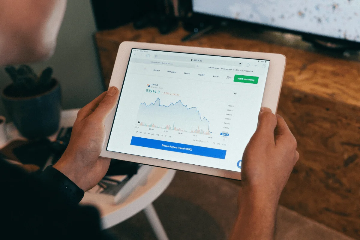A person holds a tablet displaying a Bitcoin price chart with a current value of €53,514.3 and options to buy cryptocurrency.