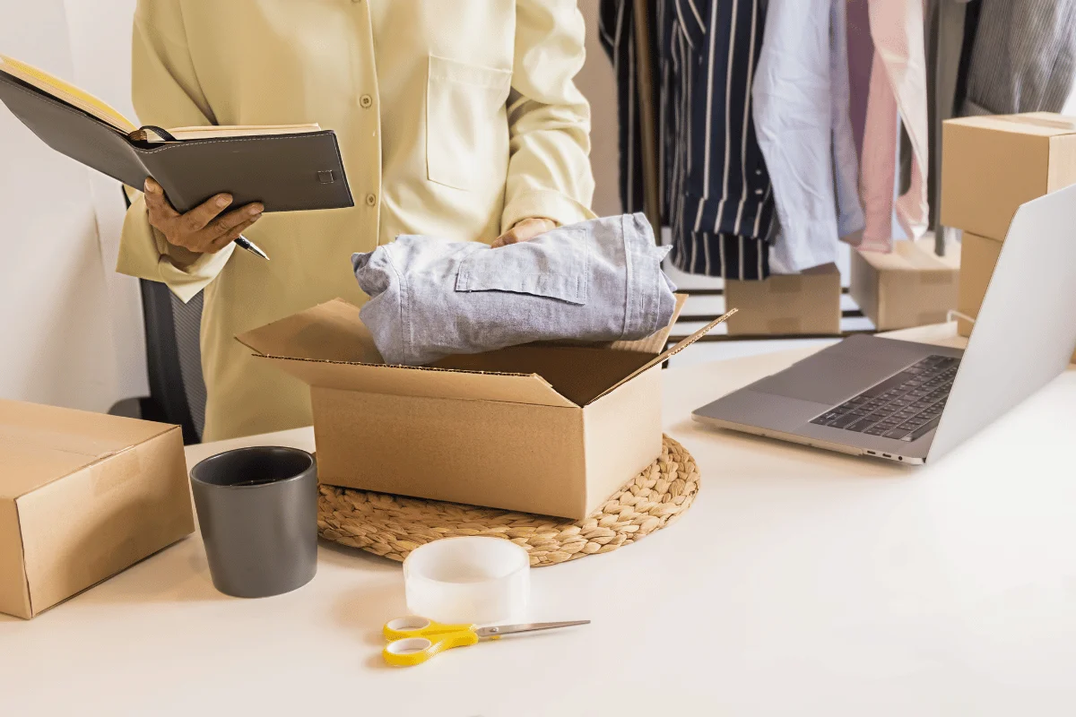 A person wrapping a shirt for shipment while writing in a notebook.