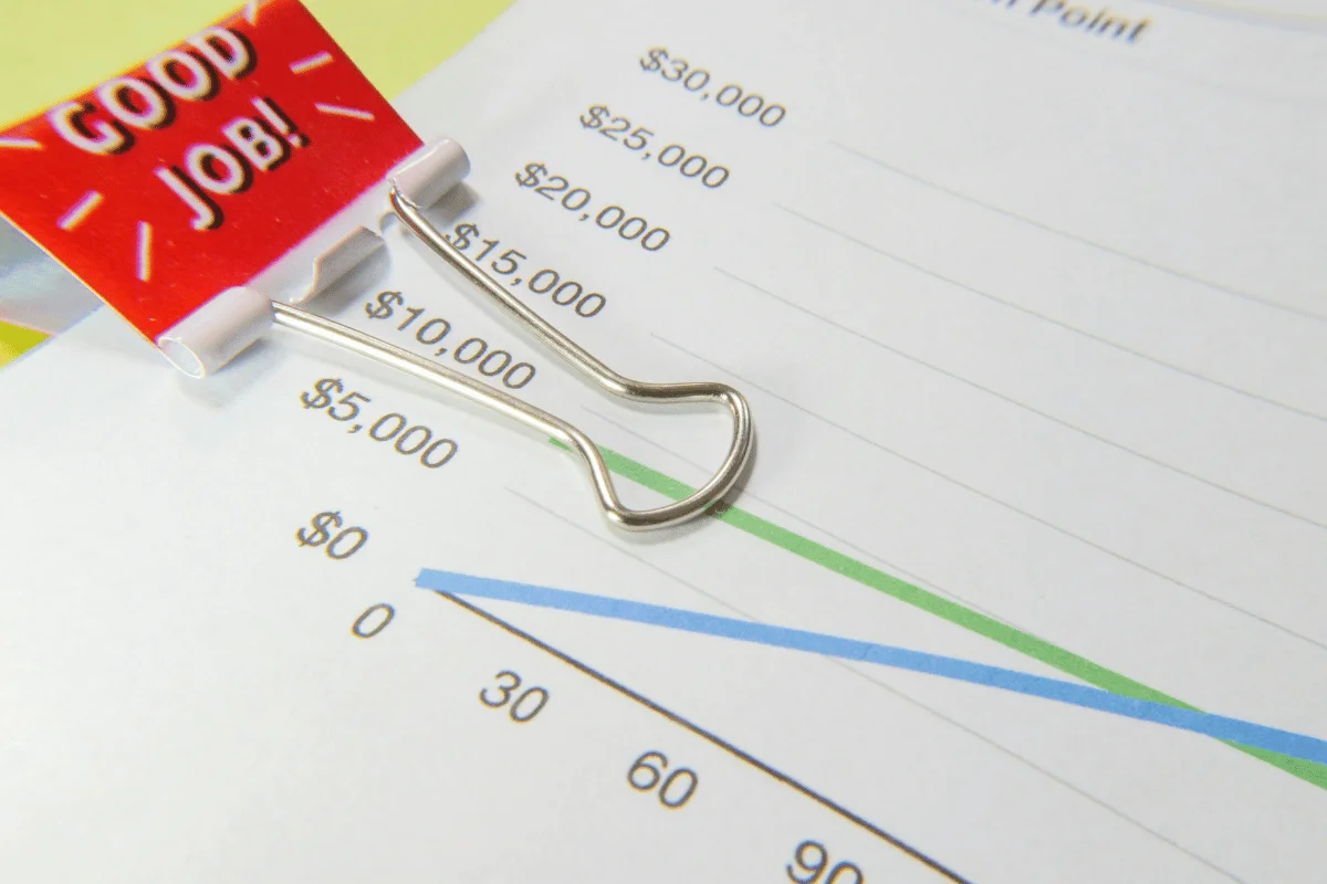 A graph sheet with blue and green lines is held by a silver binder clip with a red tag reading "Good Job!"