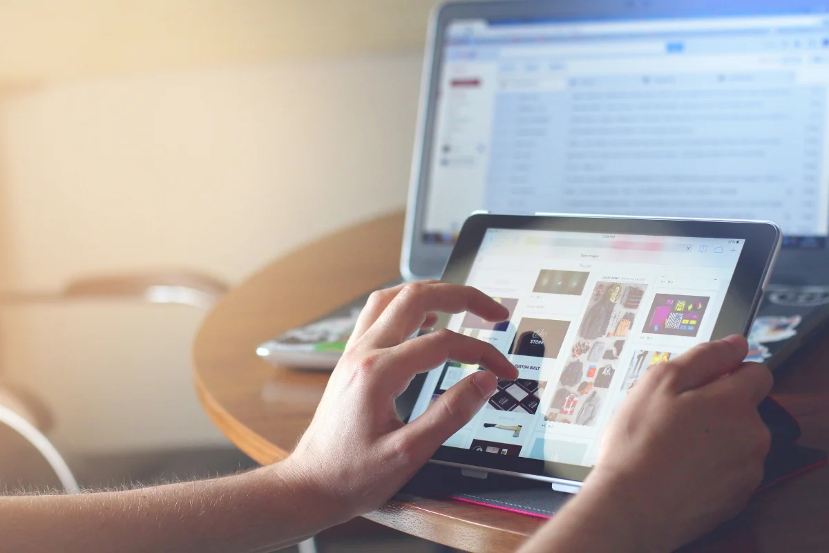 Individual browsing images on a tablet while working on a laptop.