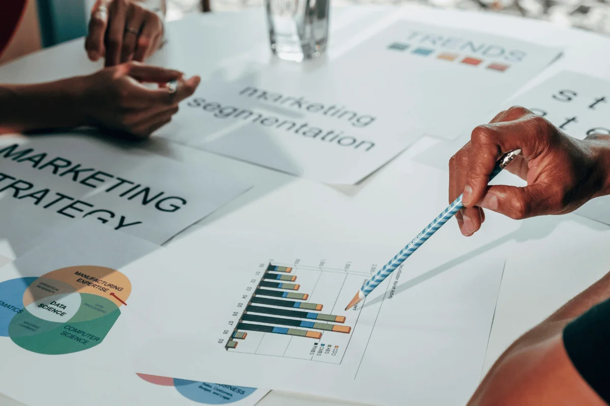 Hands pointing to marketing charts and graphs on a table, displaying a collaborative workspace focused on strategy, segmentation, and trends.