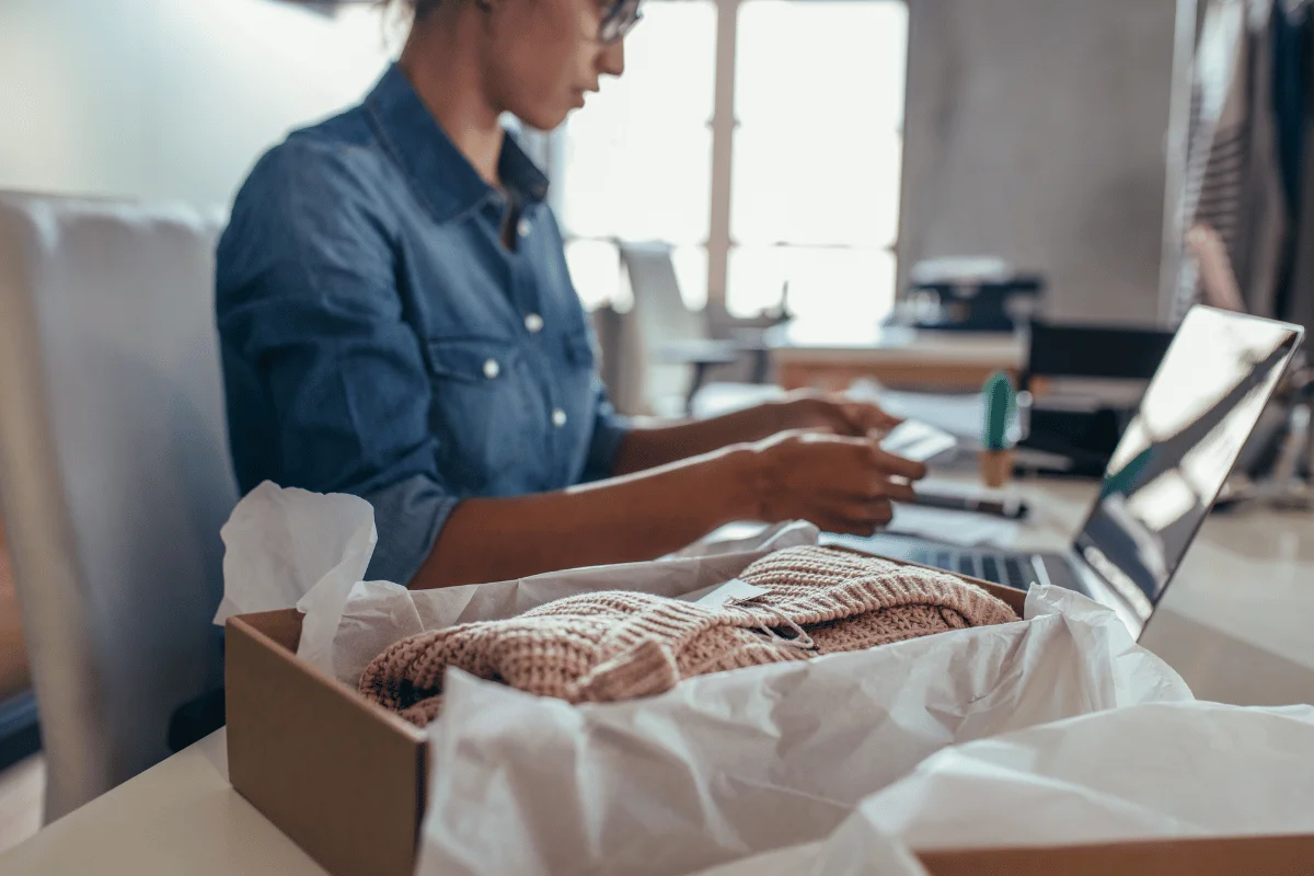 Female entrepreneur preparing a clothing package for shipment in an online business setup.