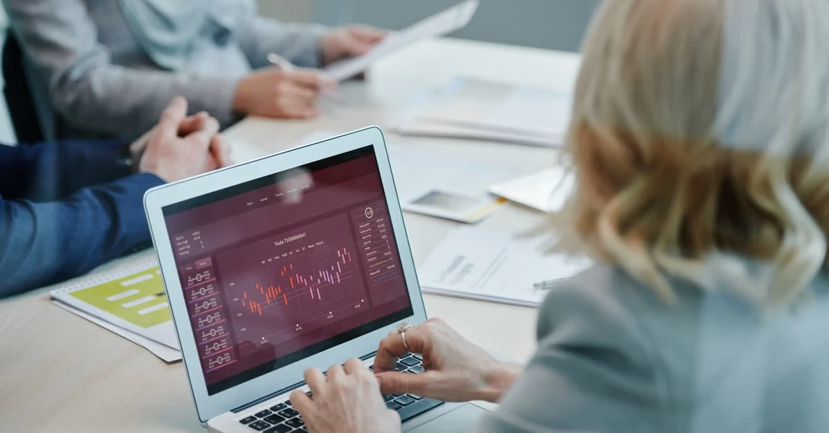 Woman analyzing tacos Amazon PPC strategy on laptop with stock charts during team meeting.